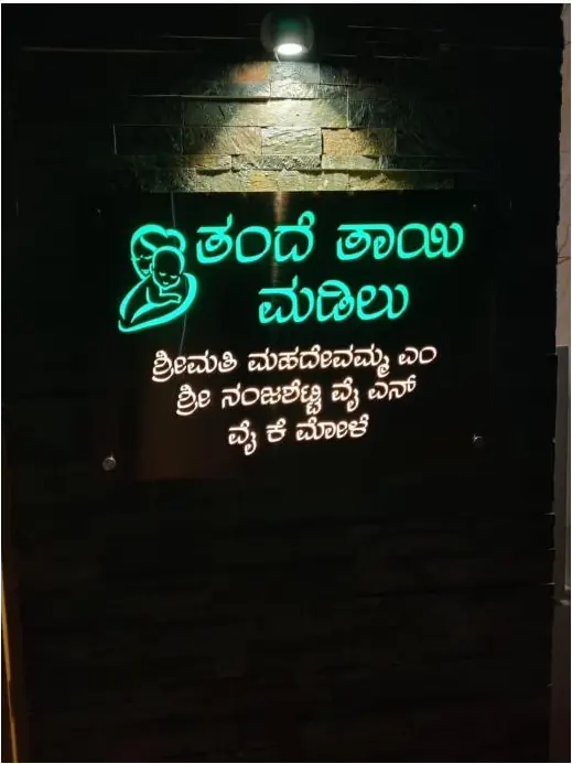 Backlit Kannada lettering on a dark wall glowing at night