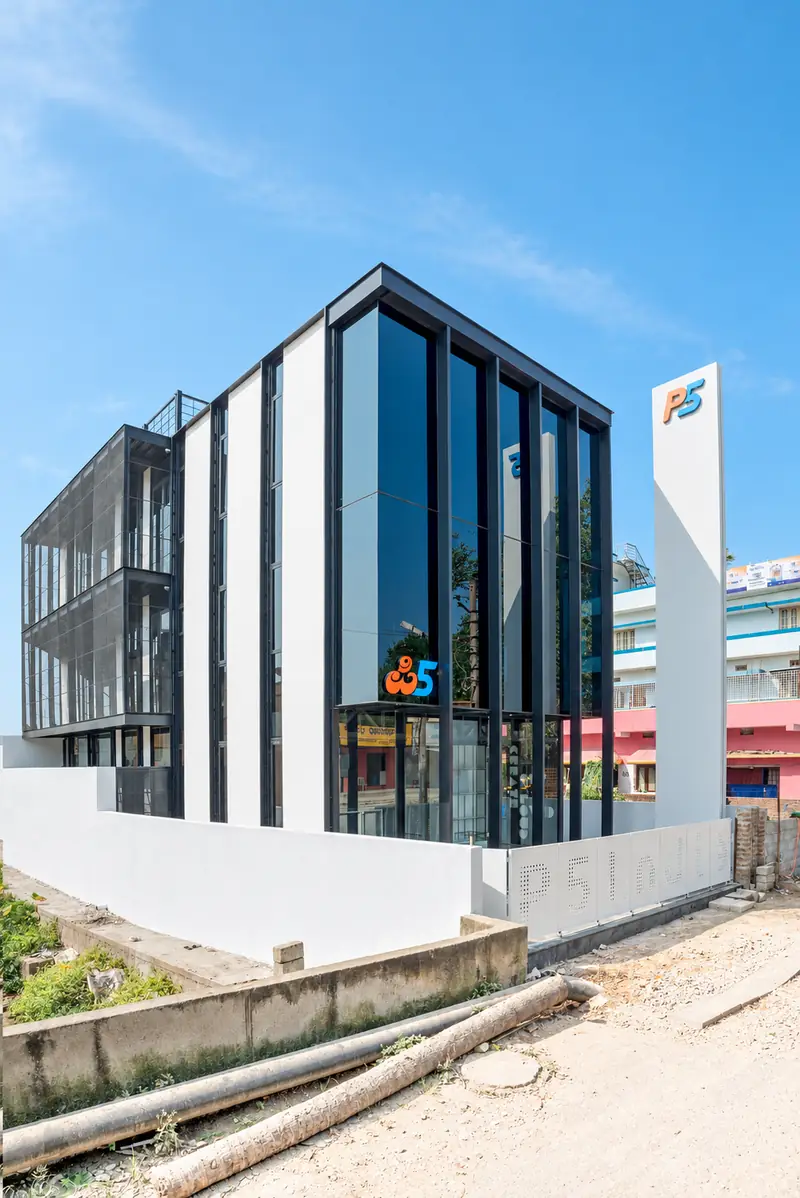 The P5 India building under a blue sky: dark glass and white fins on a corner plot, the P5 logo on the glass, and the white P5 pylon beside it