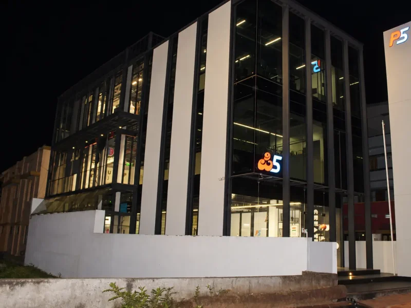 The P5 India building at night: the glass front lit from inside, the P5 logos glowing on the front and on the pylon