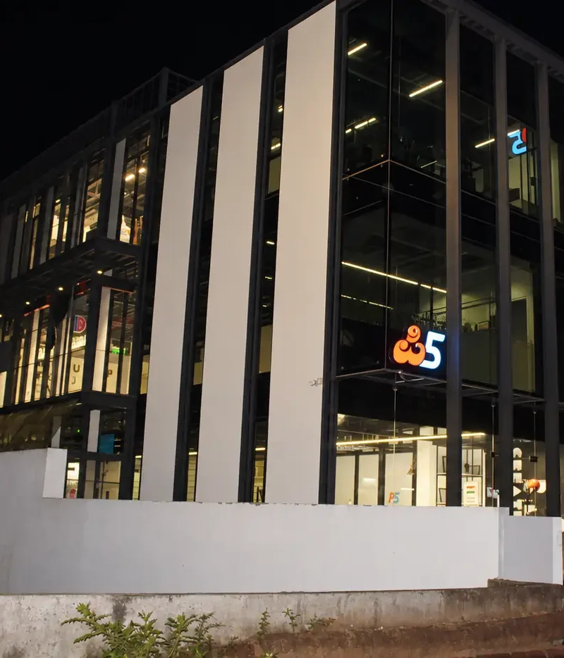 The P5 India building at night: the glass front lit from inside, the P5 logos glowing on the front and on the pylon