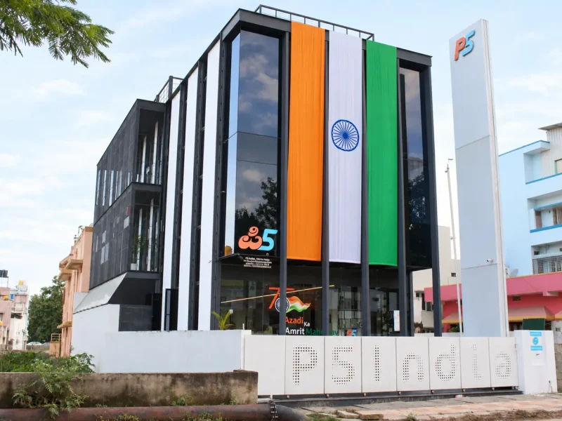 The P5 India building by day: a glass and white-fin front with a large tricolour hung down it, the P5 pylon, and P5 India cut into the compound wall