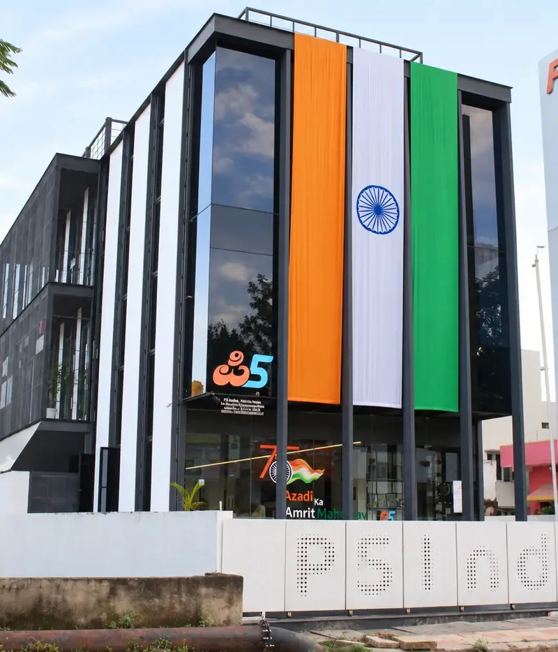 The P5 India building by day: a glass and white-fin front with a large tricolour hung down it, the P5 pylon, and P5 India cut into the compound wall