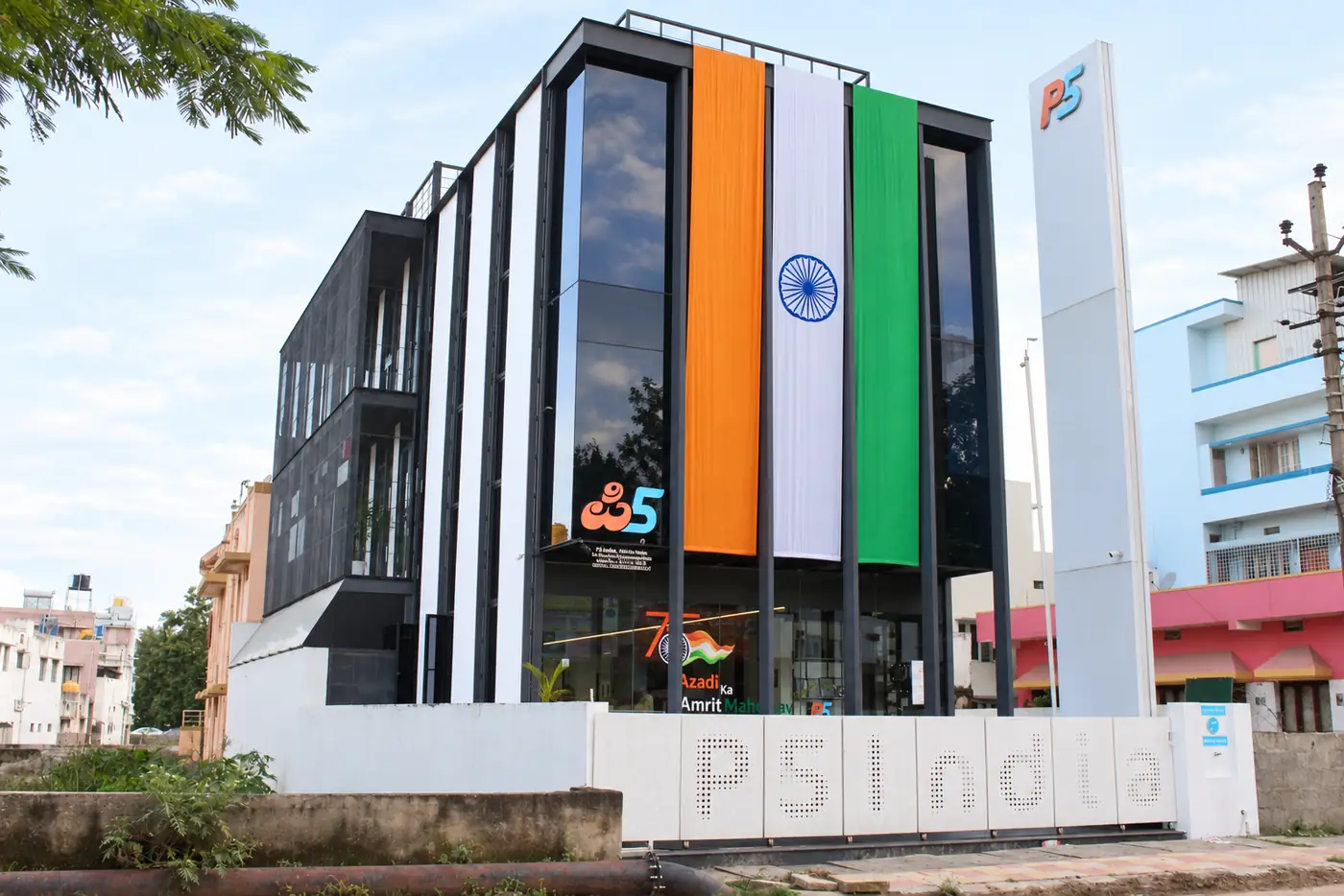 The P5 India building by day: a glass and white-fin front with a large tricolour hung down it, the P5 pylon, and P5 India cut into the compound wall