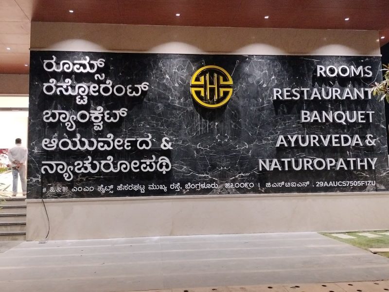 Highland Hotel feature wall with back-lit letters listing rooms, restaurant, banquet, ayurveda and naturopathy in Kannada and English