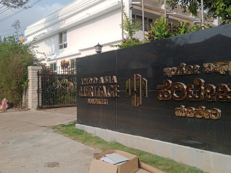 Indo Asia Heritage Madikeri in gold letters on a black granite compound wall, by day