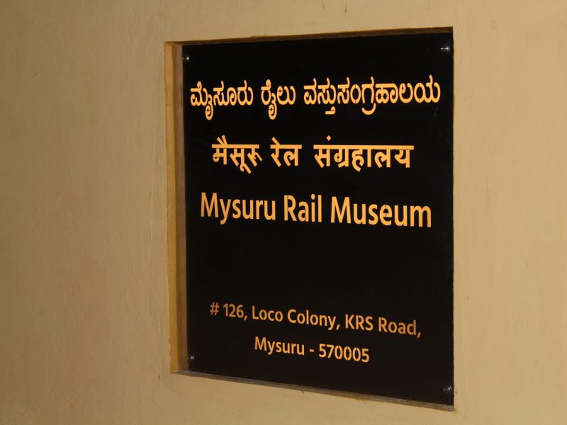 Black address plate with gold lettering reading Mysuru Rail Museum in three languages
