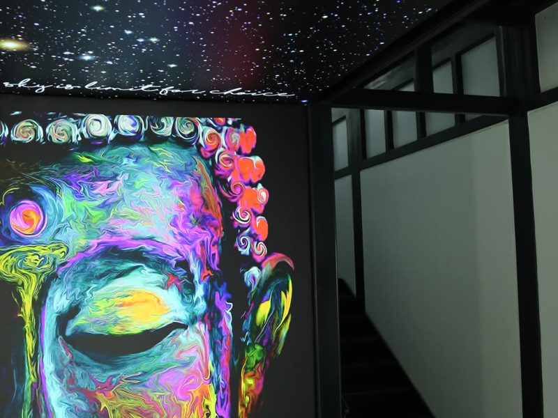 Back-lit printed panel of a multicolour Buddha face under a star-field ceiling